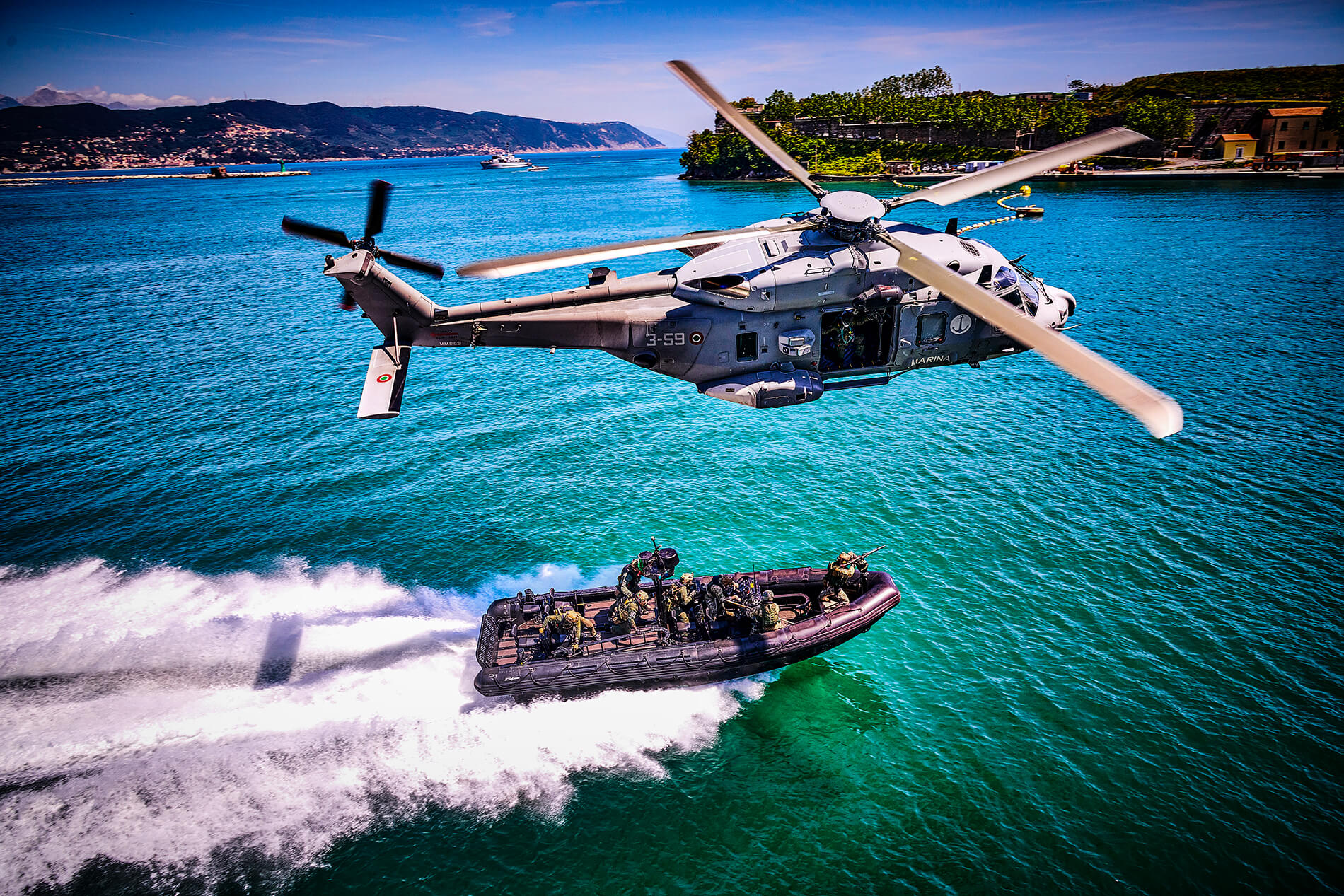 Un elicottero della Marina EH-101 sorvola un RHIB che naviga a tutta velocità con a bordo incursori